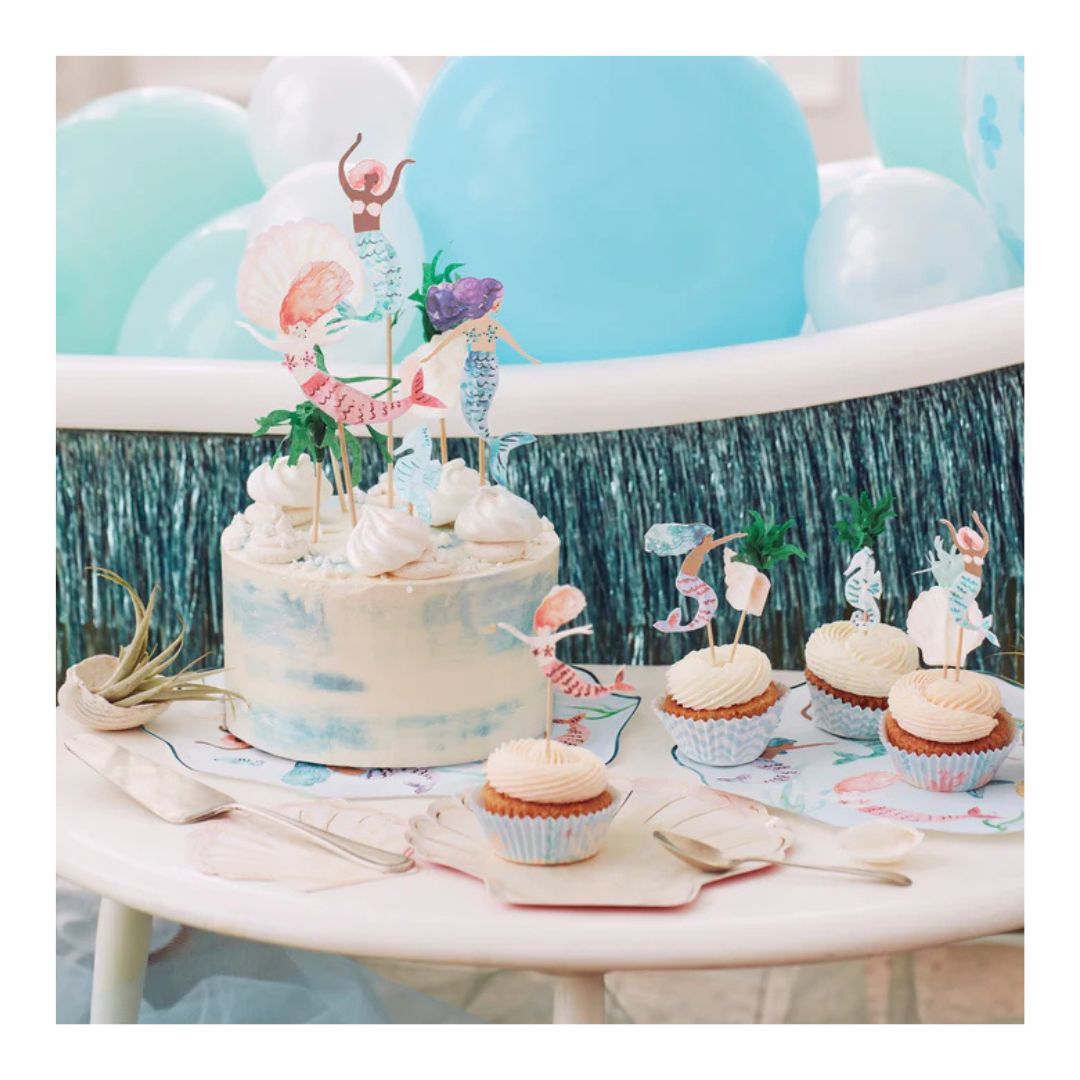 Decorative cake with cupcake toppers and balloons on a table with a blue and green backdrop. - Remarkable Parties
